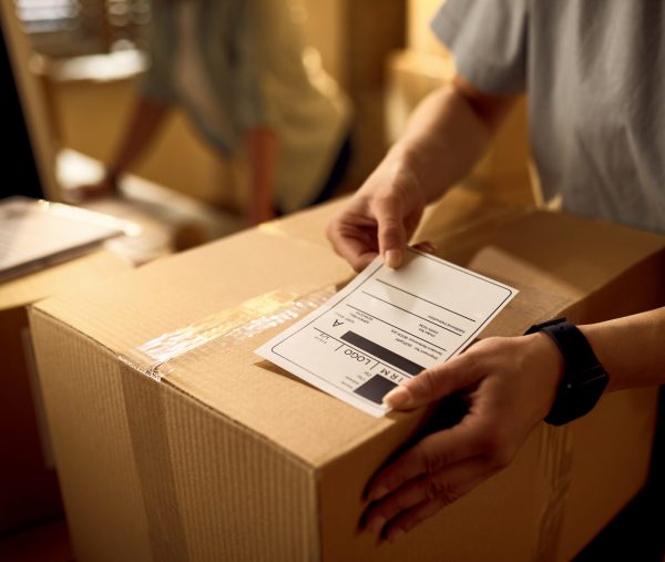 Close-up of courier attaching address label on a package while working in the office.